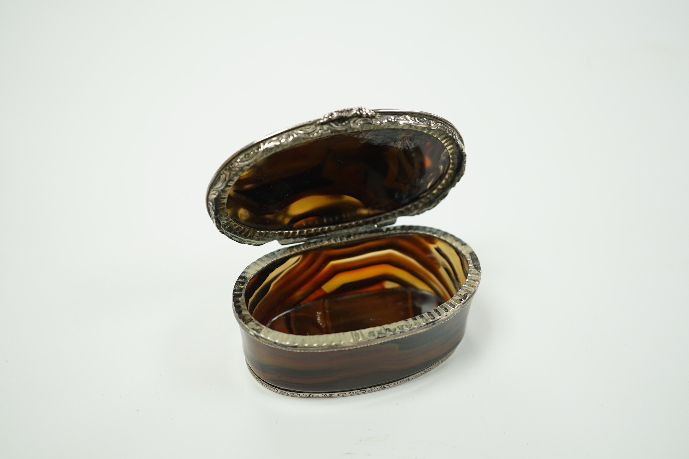 A 19th century continental white metal mounted banded agate oval snuff box, decorated with figures amid scrolls, length 79mm.
